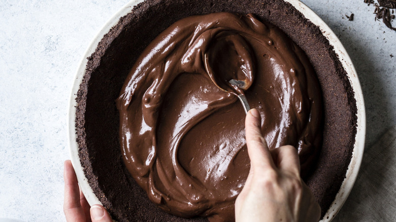 Overhead view of person filling chocolate pie crust with filling