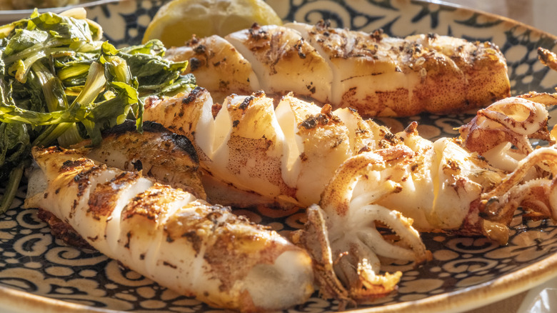 Grilled calamari on a blue and white plate with a garnish of lemon and greens