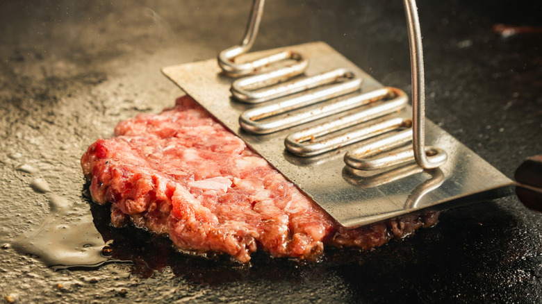 A smash patty being pressed on a hot flat-top grill.