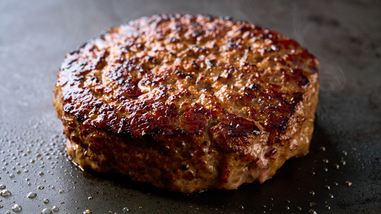 A beautifully browned and crusted burger patty on a flat-top grill.