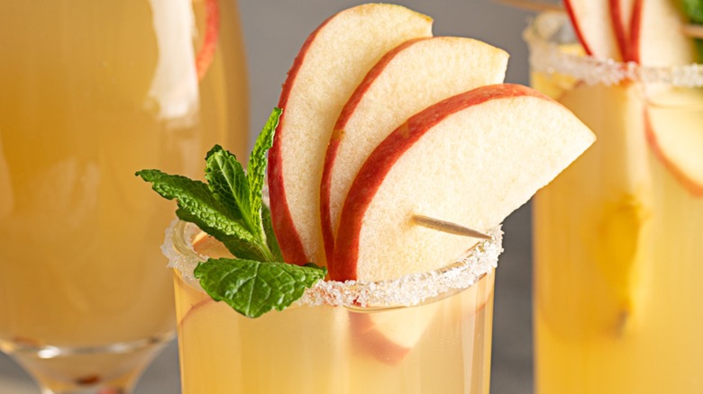 Closeup of a whiskey cocktail garnished with fresh apple slices and mint