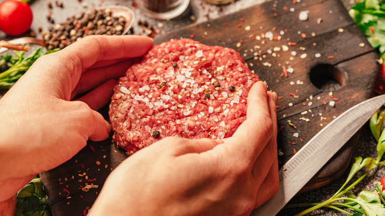 A person uses both hands to form a seasoned burger