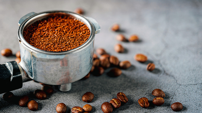fresh ground coffee in a portafilter with scattered coffee beans on a stone surface