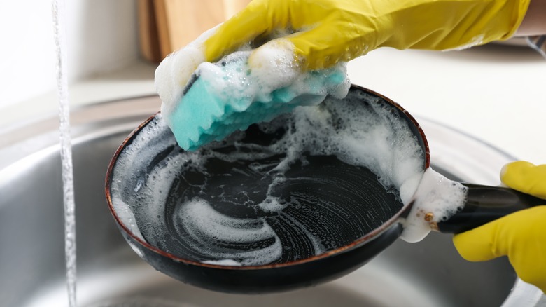 A person washing a frying pan while wearing gloves