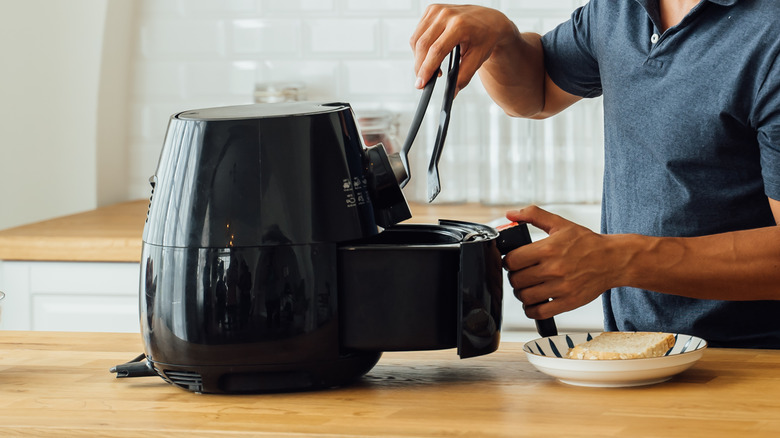 man using tongs with air fryer