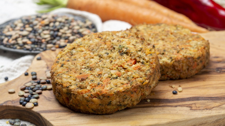 Two homemade veggie patties on wooden board with dried beans.