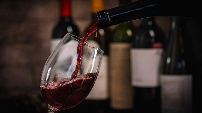 A glass of red wine poured from a bottle, with other wine bottles in the background