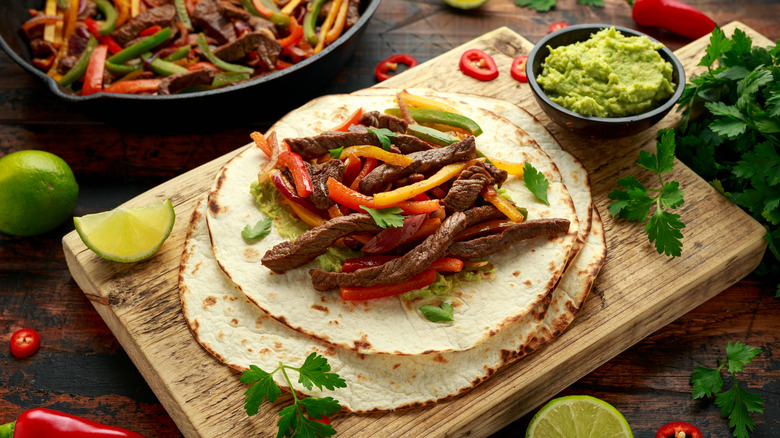 Tortillas on a wooden cutting board with meat and guacamole