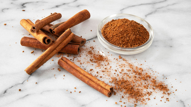 bowl of ground cinnamon with cinnamon stick beside it