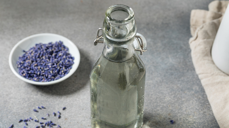 bottle of simple syrup with a bowl of lavender flowers in the background