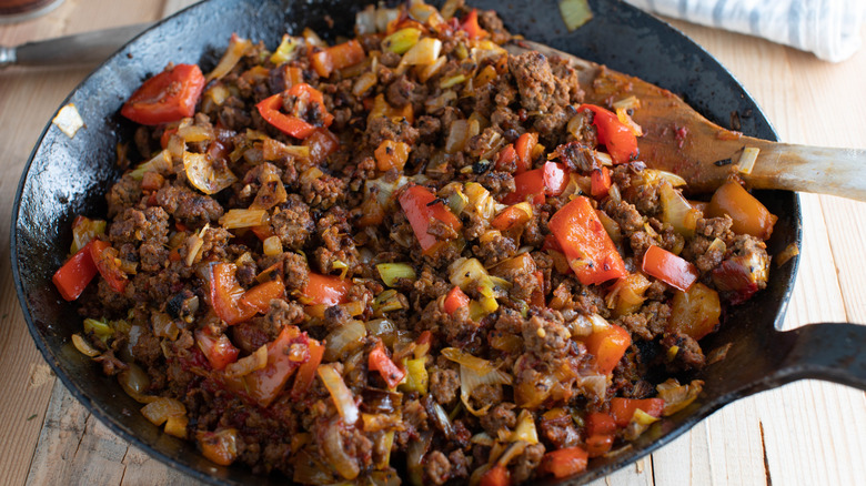A pan of sauteed beef, cabbage, and peppers sitting on a wooden table