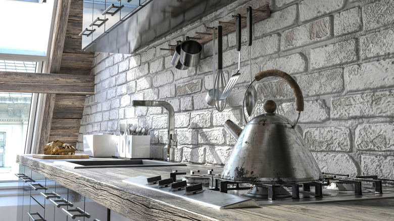 A kettle on the stove in a ktichen against a brick backsplash