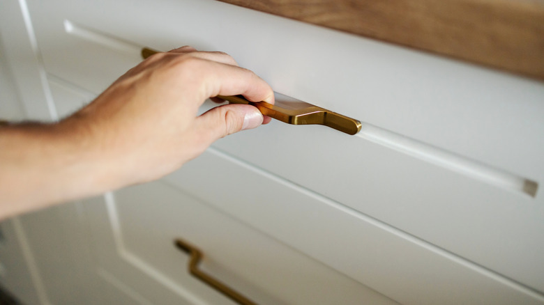 A person grabbing the handle on a kitchen drawer