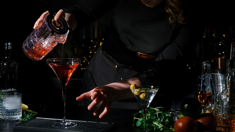 A bartender pours a sweet vermouth martini into a glass, next to dirty martini
