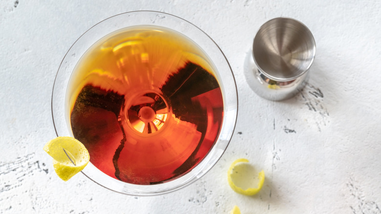 An aerial view of a martini made with sweet red vermouth with a lemon twist garnish, next to jigger