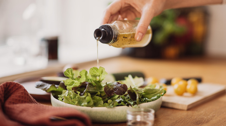Person pouring dressing bottle into bowlful of salad