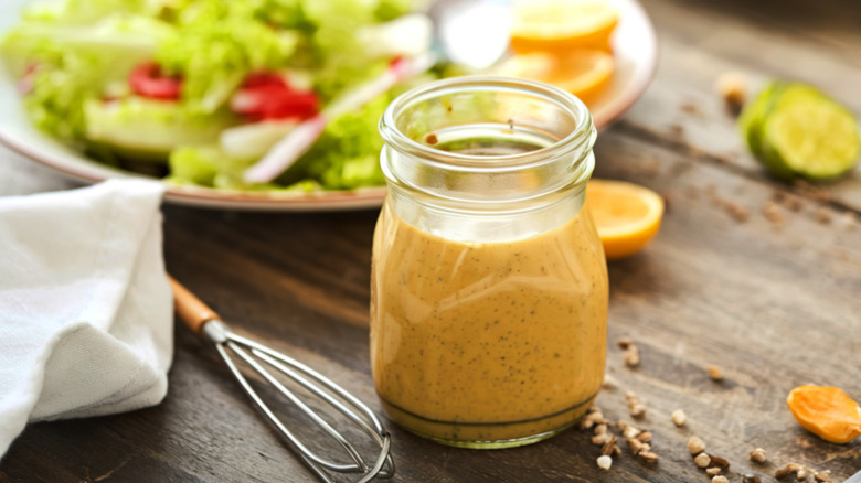 Closeup of jar of homemade mustard vinaigrette salad dressings on a table with a whisk