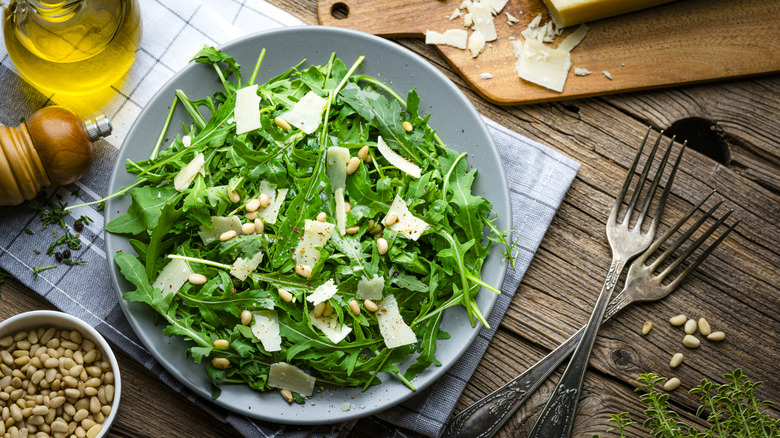 Overhead view of a salad with arugula, pine nuts, and Parmesan cheese in a bowl