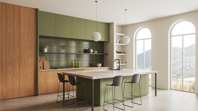 Spacious modern kitchen with olive green upper cabinets and island, and wooden lower cabinets and pantry doors.