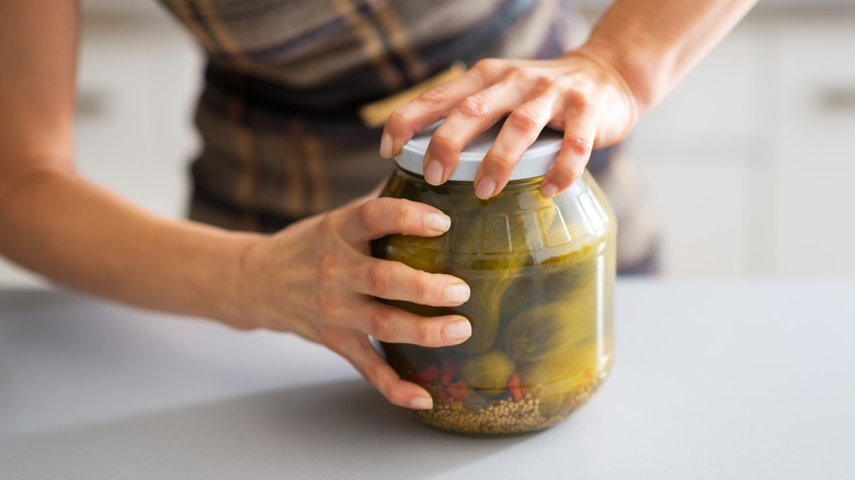 A person struggling to open a jar of pickles