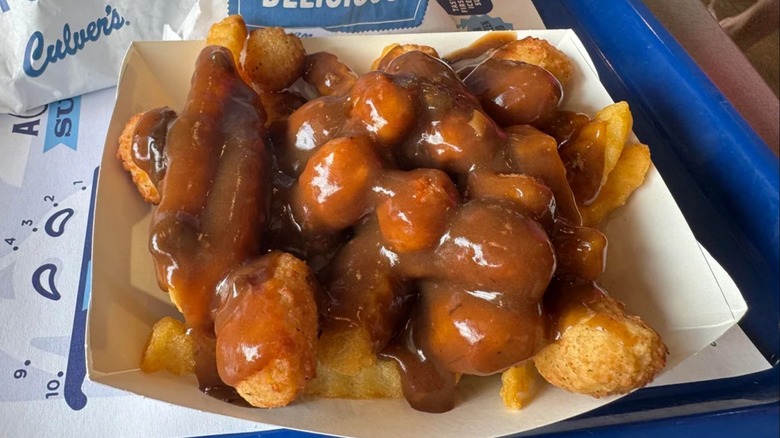 A Culver's boat with fries, cheese curds, and dark brown gravy sits on a blue tray.