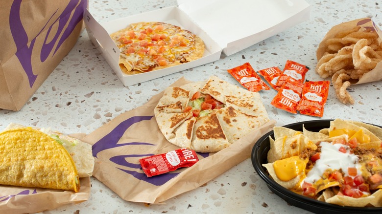 Several Taco Bell menu items including a Crunchwrap, Mexican pizza, not chose, a couple of tacos, cinnamon twists and hot sauce packets