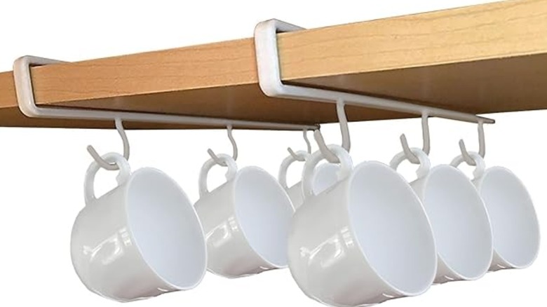 Mugs hanging on hooks underneath cupboard shelf