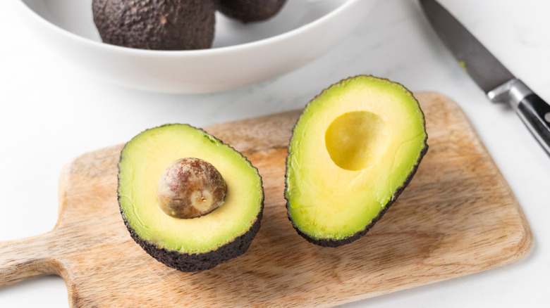 Halved avocado on small wooden cutting board