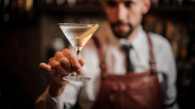 hipster bartender holds out chilled martini with lemon twist