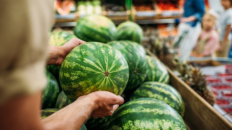 Person picks up a watermelon from a display in a grocery store