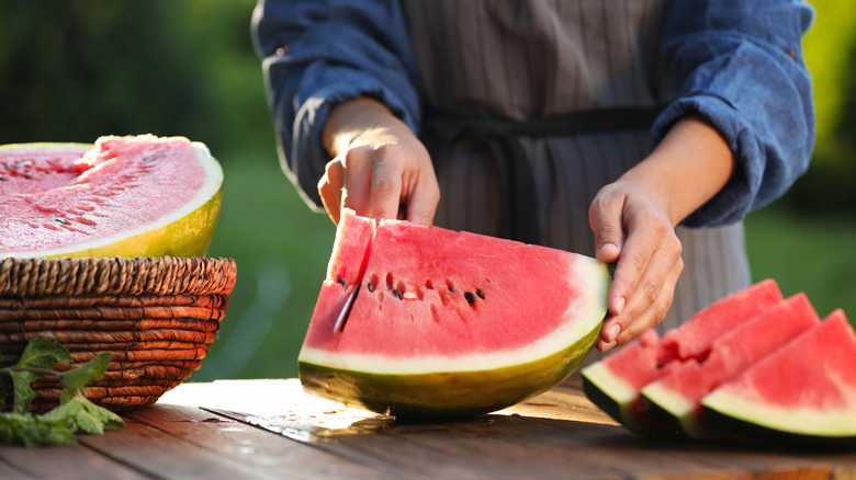Person slices a watermelon at an outdoor wooden table