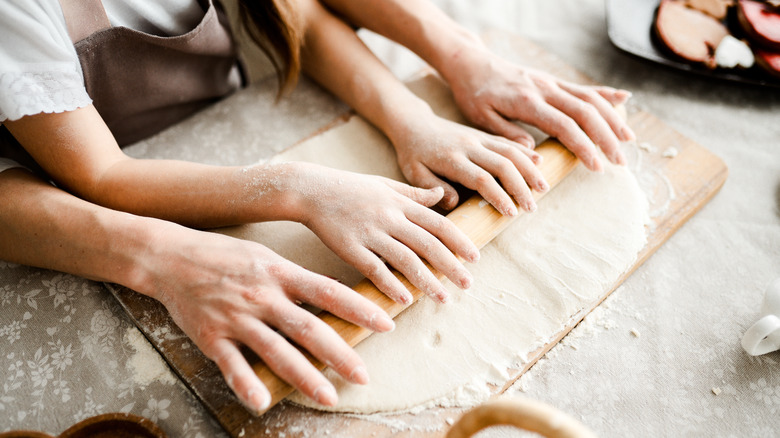 Two people rolling out dough with a rolling pin