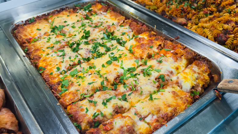 a tray of lasagna sliced into squares with chopped parsley on top in a metal tray with a spatula