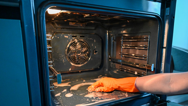 A person wearing orange rubber gloves cleaning the interior of a kitchen oven