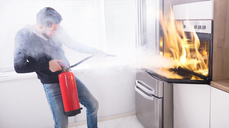 A man putting out an oven fire with a fire extinguisher