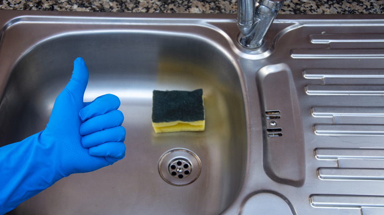 Gloved hand making "thumbs up" signal in front of kitchen sink