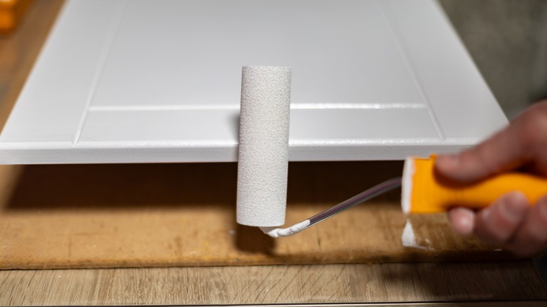 A roller being used to paint a cabinet White