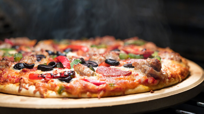 Steaming pizza on pan with pepperoni, sausage, and veggies