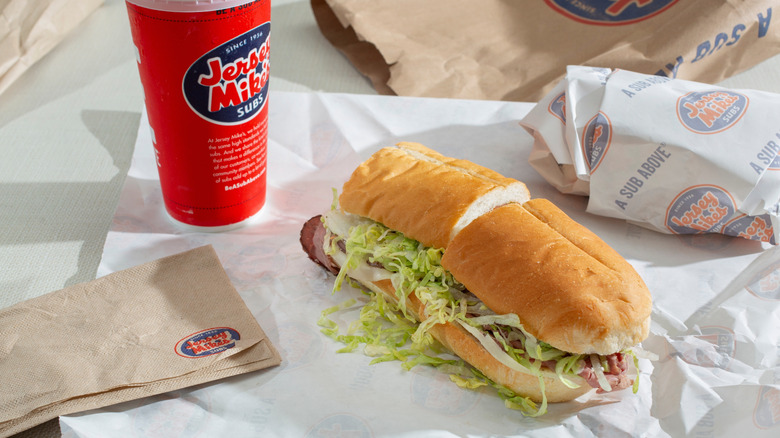 A Jersey Mike's combo meal, including an unwrapped Italian sub sandwich next to a branded drink cup next to a Jersey Mike's bag and wrapping paper