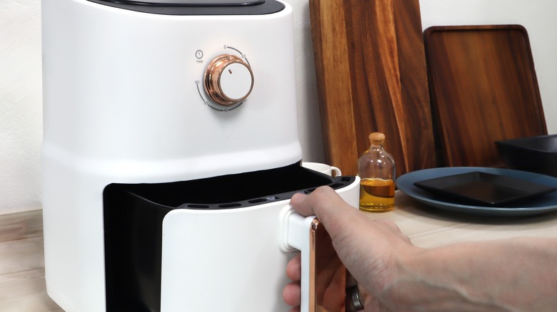 A person reaching to open a white air fryer.