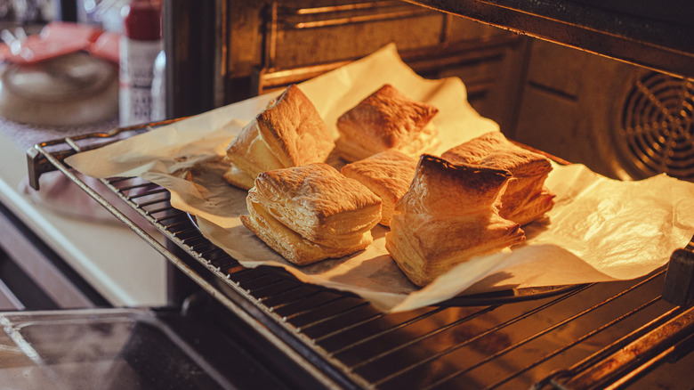 Puff pastry baking on parchment-lined pan in the oven rack