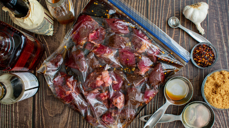 Raw beef marinates in a plastic bag sitting on a wood table, surrounded by ingredients