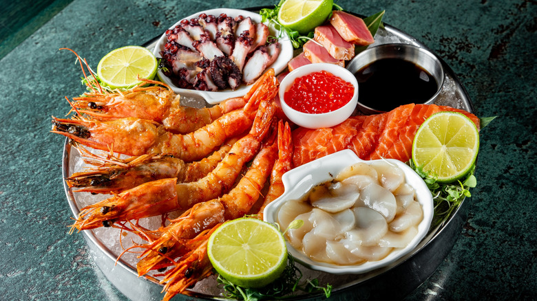 A platter of various seafood on ice in a round metal tray with high sides