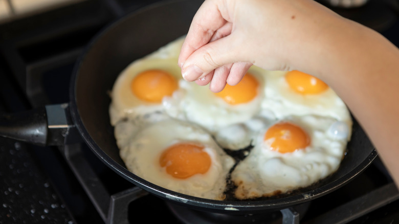 adding salt to pan of fried eggs