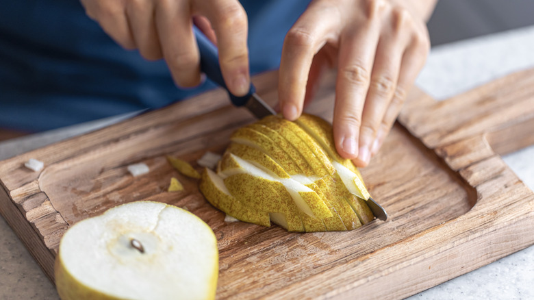 Hands slicing pear on cutting board