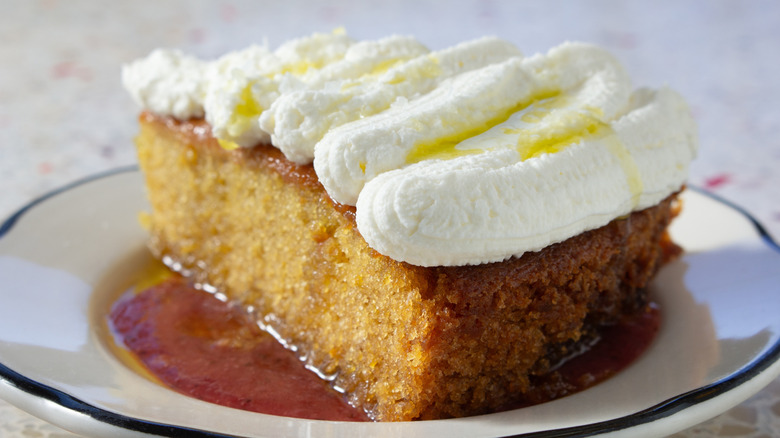 Slice of cake with white frosting and olive oil on white plate
