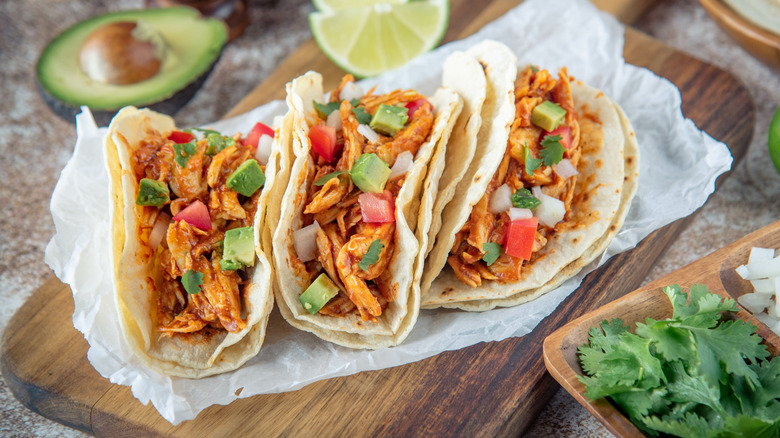 Shredded chicken, avocado, and tomato tacos on parchment-lined wooden board