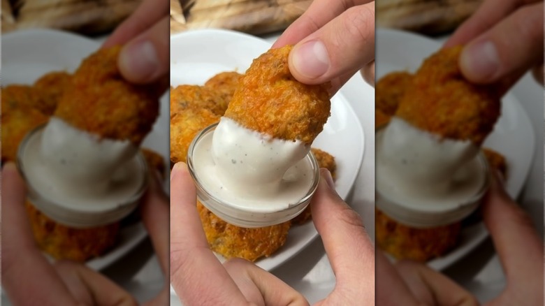 Hand dunking chicken nugget into pot of creamy dip