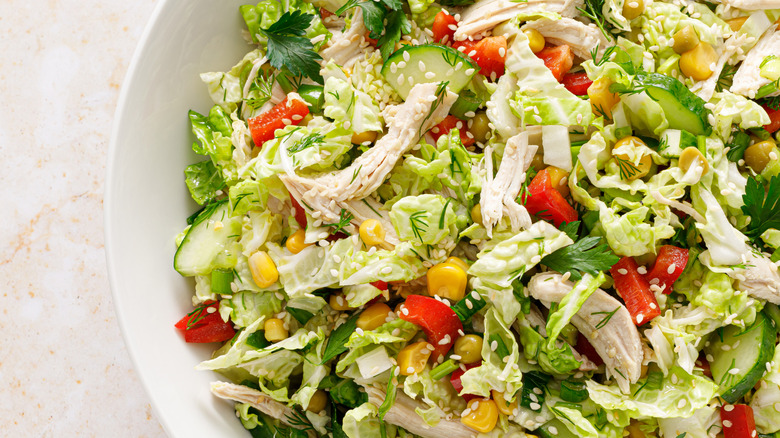 Close up of bowl of shredded chicken salad with cabbage, cucumber, and corn