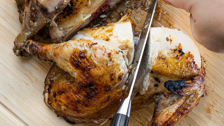 Hand slicing whole roasted chicken with knife